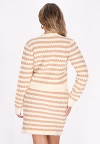 Vestido de punto a rayas beige con una textura suave, que presenta puños y dobladillo acanalados. El diseño muestra rayas alternas claras y oscuras.