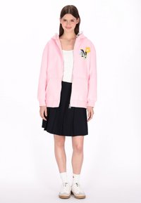 Hellrosa Zip-Up-Hoodie mit floraler Stickerei, ausgestattet mit Kapuze, Kängurutaschen und gemütlichem Material, kombiniert mit einem schwarzen plissee Rock.