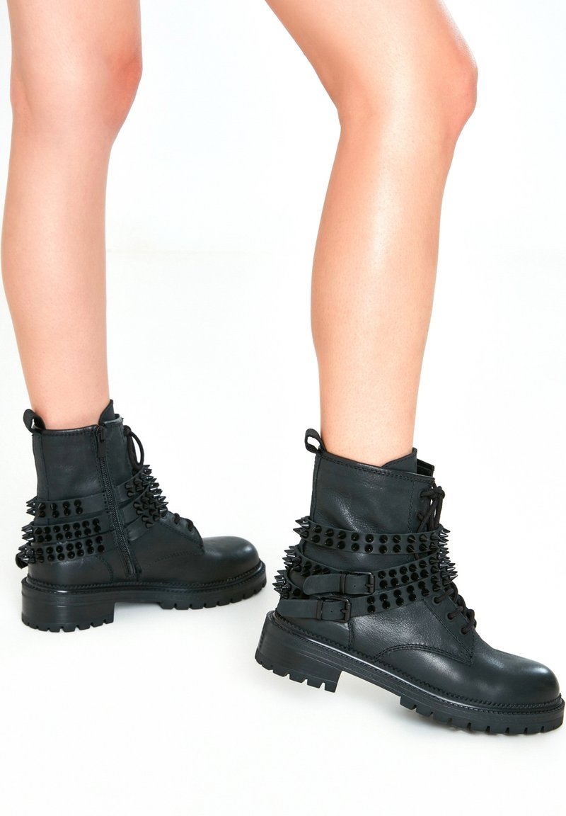 Svarta läderankelstövlar med nitar, en kraftig sula och spännen, med snörning och dragkedja på sidan.