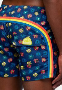 Pantaloni da bagno con un vivace motivo di sole e faccine sorridenti in colori brillanti, dotati di una tasca laterale e dettagli a strisce colorate.