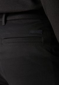 Pantalon noir avec une surface texturée, doté d'une poche arrière et d'une étiquette Calvin Klein cousue en noir. Design slim fit avec des lignes épurées.