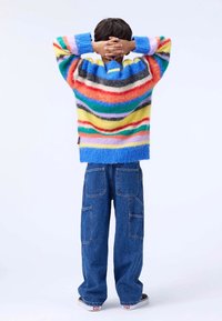 Multicolored, striped sweater with fluffy texture, featuring blue cuffs. Paired with loose-fit denim cargo pants with multiple pockets.