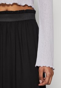 Lichtpaarse top met lange mouwen, geribbeld, met gegolfde zoom, gecombineerd met een zwarte rok met een geplooide tailleband.