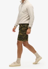Sudadera cremosa con cremallera, pantalones cortos de camuflaje con bolsillos, zapatillas de deporte de color claro y calcetines beige. Diseño sencillo, estilo casual.