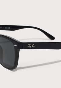 Ochelari de soare Ray-Ban negri cu lentile rectangulare, cadru solid negru și logo argintiu pe bradă. Prezintă lentile întunecate și un design clasic.