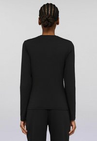 Maglietta nera a maniche lunghe con un design aderente, texture liscia, scollatura rotonda e cuciture piatte. Indossata con pantaloni neri coordinati.