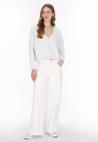 Un pull court gris clair avec un col en V, associé à un jean blanc à taille haute et à jambes larges. Des baskets décontractées complètent la tenue.