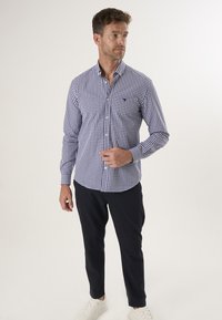 Blauwe en witte geblokte blouse met lange mouwen, gemaakt van geweven stof, gecombineerd met marineblauwe broek en witte sneakers.