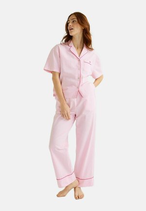 Femme debout pieds nus portant un haut de pyjama à manches courtes rayé rose et blanc et un pantalon large assorti avec des détails de passepoil rouge.