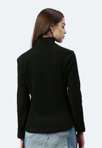 Giacca in fleece nera con colletto rialzato e maniche lunghe, caratterizzata da un tessuto texturizzato e una silhouette aderente, abbinata a una gonna di jeans.