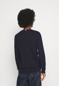 Maglione a treccia navy con maniche lunghe, polsini e orlo a coste. Presenta un piccolo accento tricolore sul collo posteriore.