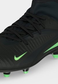 Μαύρο ποδοσφαιρικό παπούτσι Nike με πράσινες λεπτομέρειες, κορδόνια και τάπες σχεδιασμένο για βελτιωμένη πρόσφυση στο γήπεδο.