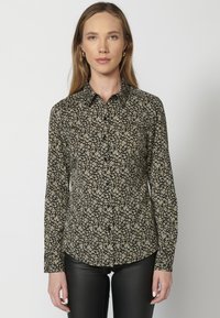Camicia nera con bottoni, decorata con piccoli motivi floreali bianchi e gialli, maniche lunghe e colletto, realizzata in un tessuto morbido.