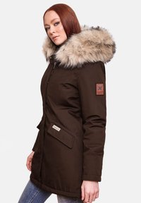 Bruine parka jas met een grote nep bont capuchon, ritssluiting, voorzakken en logo patch op de mouw. Glad stoftextuur, middellange lengte.