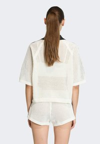Biele sieťované tričko s krátkym rukávom a voľným strihom, s rebrovaným lemom a výstrihom. V kombinácii s bielymi sieťovanými šortkami. Pohľad zozadu.
