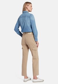 Lichtblauwe denimbloes, tan kleurige cargobroek met zijzakken en witte sneakers. De blous heeft een kraag en knoopsluiting bij de mouwen.