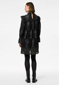 Černé šaty s květinovým vzorem, volánkovými rukávy a detaily na zádech ve tvaru klíčové dírky. Stylizované s neprůhlednými černými punčochami a robustními černými botami.