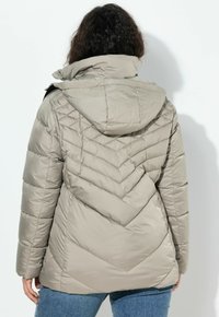 Giubbotto imbottito beige con cappuccio, caratterizzato da un design a zig-zag. Dotato di tasche laterali e polsini elasticizzati per il calore.