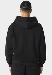 Sudadera negra con capucha, hecha de una tela suave. Presenta puños y dobladillo acanalados, con un diseño minimalista y sin logotipos visibles.