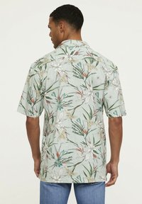 Chemise à manches courtes en tissu vert clair avec une impression florale, mettant en avant de grandes fleurs crème et des feuilles vertes, coupe décontractée avec un ourlet droit.