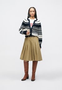 Ναυτικό και λευκό ριγωτό ζακέτα πάνω από λευκό μπλουζάκι με σχέδιο, συνδυασμένο με πλισέ χακί φούστα και καφέ δερμάτινα ψηλοτάκουνα μπότες μέχρι το γόνατο.