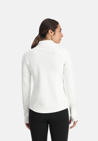 Pull en blanc à manches longues avec un col montant, en tissu texturé, coupe ajustée et accents sans couture, associé à des leggings noirs.