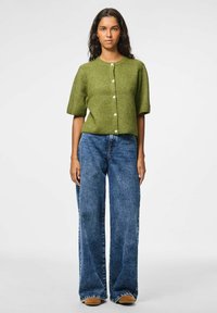 Cardigan court en tricot vert à manches courtes avec un col rond et une fermeture à boutons, associé à un jean en denim bleu à jambes larges et des chaussures marron.