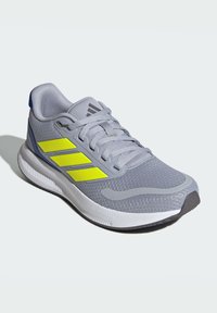 Zapatilla atlética gris con parte superior de malla, tres rayas amarillas, suela Cloudfoam y acentos texturizados con un talón azul.