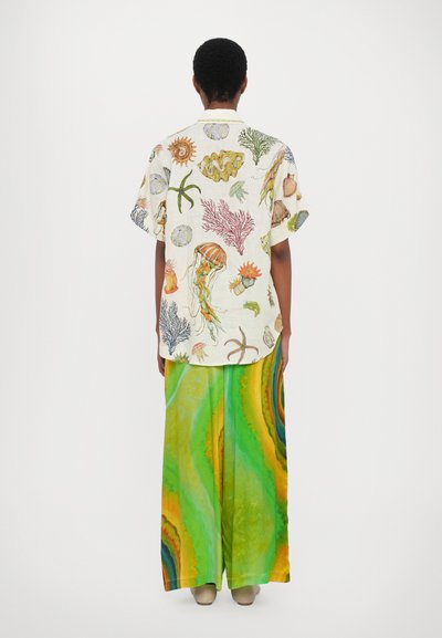 Camicia a maniche corte color crema decorata con stampe a tema marino multicolori; abbinata a pantaloni larghi con gradiente verde e giallo.