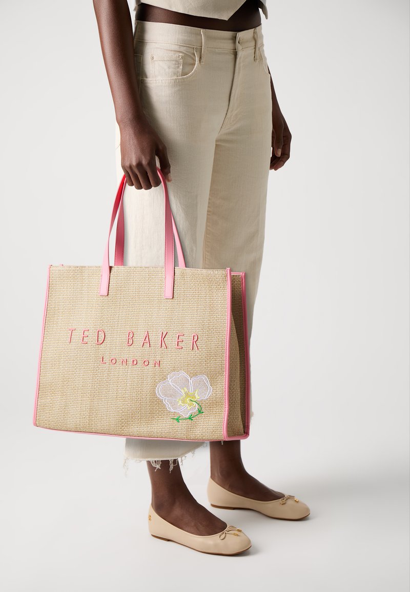 Beige gewebte Tragetasche mit pinkfarbenen Griffen. Mit pinkfarbenem Schriftzug "TED BAKER LONDON" und floralen Stickereien. Flaches Design mit offenem Oberteil.