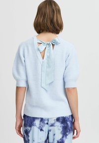 Hellblauer, gestrickter Pullover mit einem V-Ausschnitt hinten, satinierter Bindung und kurzen Puffärmeln. Der Stoff hat eine weiche, strukturierte Oberfläche.