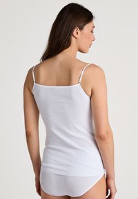 Débardeur en coton blanc avec des bretelles fines, présentant un design simple et une texture lisse, porté avec un shorty blanc assorti.