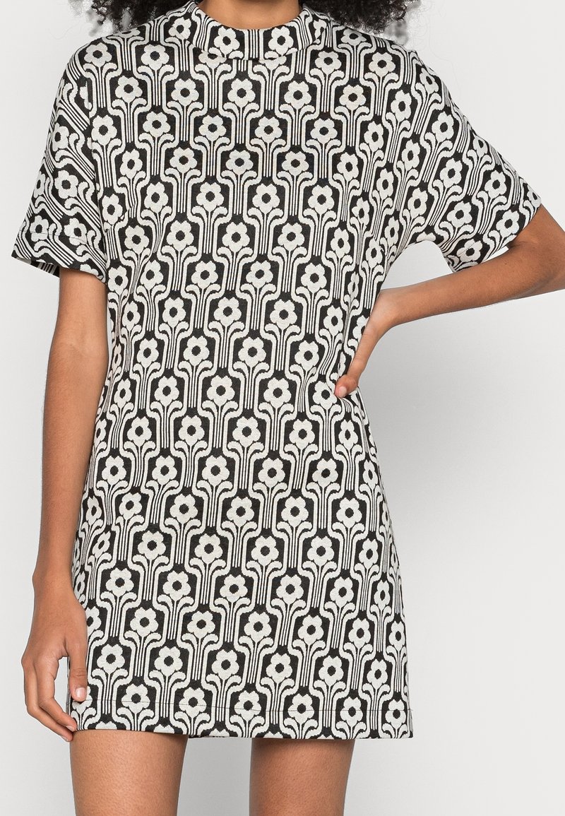 Schwarzes und weißes Kurzarmkleid mit floralem Muster und vertikalen Stängeln, hohem Ausschnitt und lockerer Passform. Weiche Stofftextur.