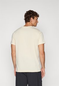 Krémové tričko s krátkým rukávem, kulatým výstřihem, vyrobené z měkké bavlny, volného střihu a s minimálními detaily šití na švech.