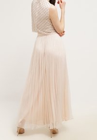 Lång plisserad klänning i ljusrosa tyg med en figursydd midja och ärmlös, texturerad överdel med ett diamantmönster och pärlbroderi.