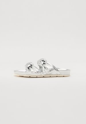 Silver flat sandals with knotted straps, smooth metallic finish, cushioned white sole, and open-toe design.