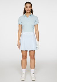 Vaaleansininen poolopaita, jossa on käännetyt hihat, yhdistettynä pleated-vaaleansiniseen hameeseen, jossa on hillitty kuvio ja valkoinen elastinen vyötärönauha.