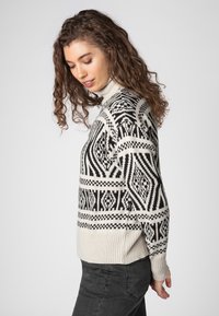 Strickrollkragenpullover in Creme und Schwarz mit geometrischen Mustern, gerippten Bündchen und Saum. Weiche Textur mit lockerer Passform.