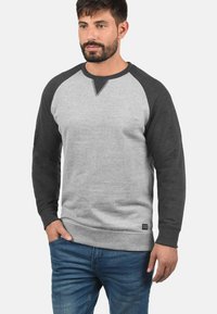 Felpa grigia e nera con maniche raglan, texture a maglia e orlo accentato. Presenta un dettaglio a V sul colletto. Vestibilità classica.