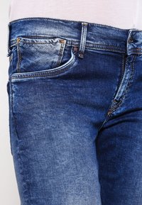 Blå jeans i denim med en urblekt tvätt, design med fem fickor, kontrasterande sömmar och en slät textur. Har dragkedja och knappstängning.