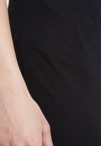 Tela negra con una textura suave, de diseño ligeramente ajustado. Una mano toca la tela, enfatizando la elasticidad y suavidad del material.