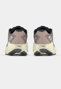 Ζευγάρι μπεζ και μαύρα αθλητικά παπούτσια με χοντρές κρεμ σόλες, εμφανιζόμενα από πίσω, με σημάδια "energy evo foam" και "GRVL".