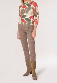 Multicolored knitted sweater with abstract patterns, paired with brown checkered pants and taupe suede knee-high boots.