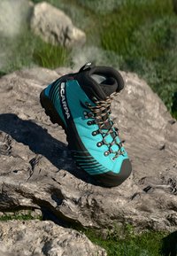 Bota de caminhada turquesa com pormenores em preto, materiais duráveis, solas texturizadas e atacadores com padrão. Projetada para uso ao ar livre em terrenos difíceis.