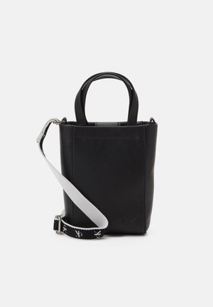 Pieni musta nahkainen olkalaukku, jossa on kaksi kahvaa ja säädettävä mustavalkoinen olkahihna, jossa on "ck"-logot.