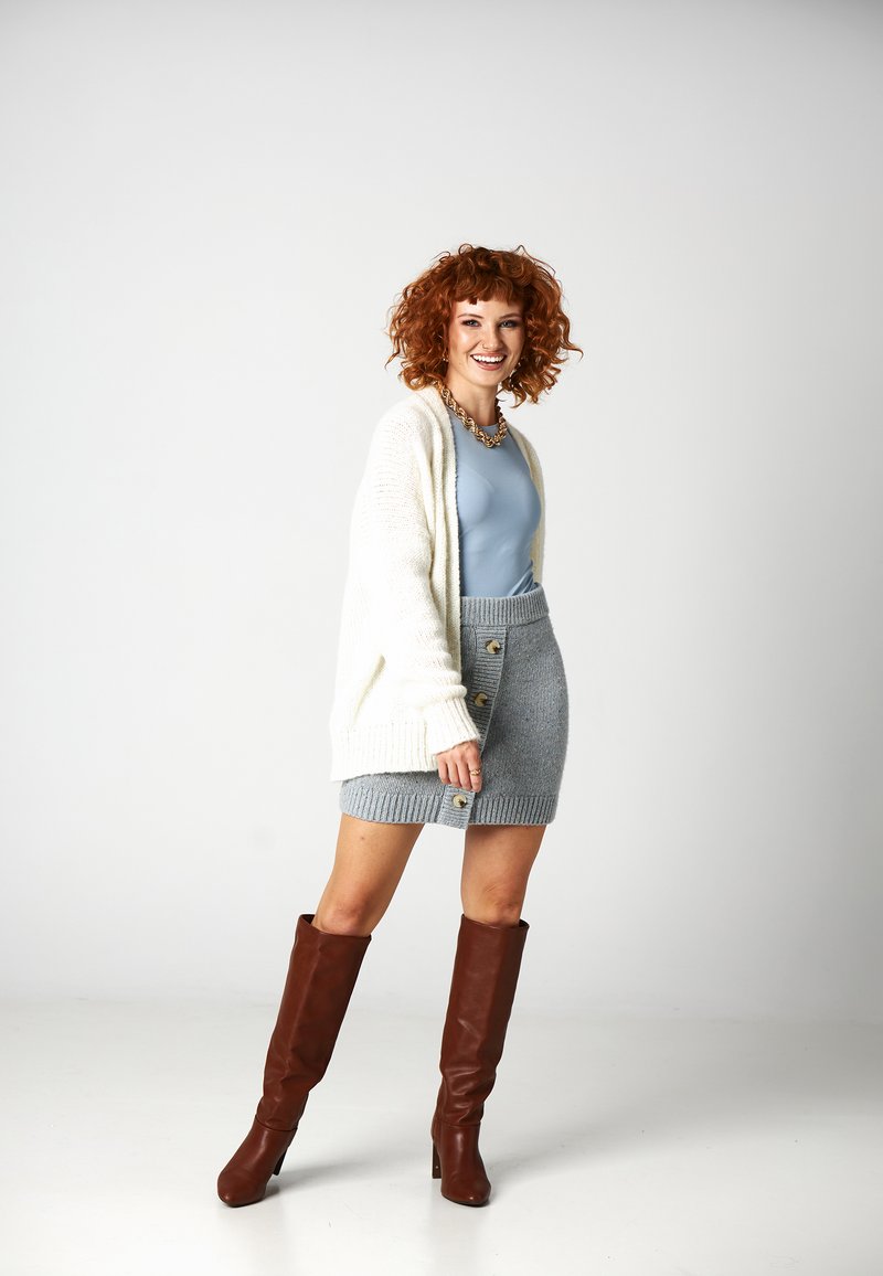 Kremowy sweter z dzianiny, jasnoniebieski dopasowany top, szara dzianinowa spódnica z guzikami i brązowe kozaki do kolan. Gładkie tekstury i warstwowy design.