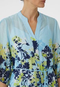 Hellblaues florales Kimono mit marineblauen und grünen Blumenmustern. Verfügt über einen gebänderten Kragen und einen Taillengürtel. Semi-transparente Stoffqualität.