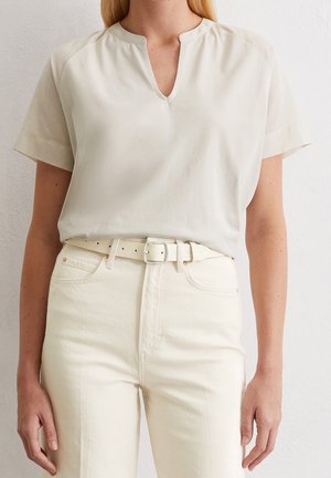 Top de manga corta beige claro con diseño de escote en V y tela ligeramente texturizada, combinado con pantalones de talle alto en color blanco roto y un cinturón a juego.