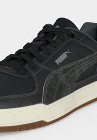 Baskets Puma noires en cuir texturé, lacets noirs, semelle intermédiaire blanche et semelle extérieure marron, avec le logo Puma sur le côté et la languette.