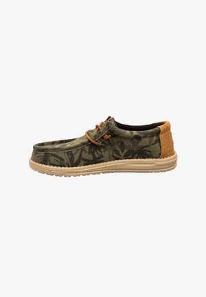 Canvas-Schlüpfschuh in Grün mit einem Blättermuster, featuring braunen Schnürsenkeln und einem strukturierten hellbraunen Absatz. Sohle aus Naturkautschuk mit Grip-Details.